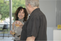 a woman with dark hair and man with grey hair stand and chat with a glass of wine in their hands. They are enjoying the museum member reception in the Link Gallery outside Krannert Art Museum.