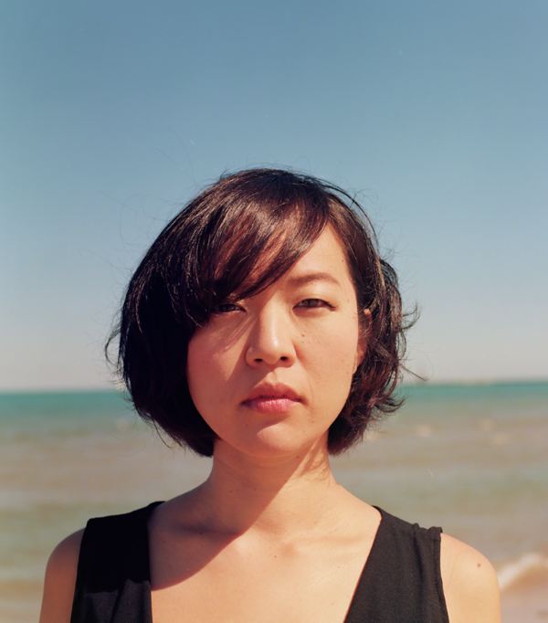 Image of Mai Sugimoto standing at the shore of a beach on a cloudless day with the sun shining onto her face.