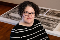 Image of Krannert Art Museum's new exhibition Fake News & Lying Pictures curator Maureen Warren with curly hair wearing a pair of black and brown striped glasses as well as a black sweater with white horizontal lines.