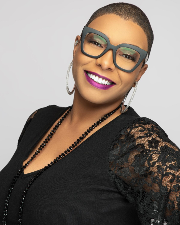 Image of Dr. Kelli Morgan smiling at the camera wearing a black blouse with floral mesh sleeves and a black beaded necklace paired with silver hoop earrings.