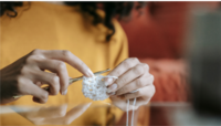 adult hands holding a partly crocheted white yarn piece with a needle in the other hand, crocheting.