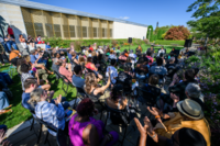 Image of a large crowd seated in black folding chairs on the Krannert Art Museum lawn listening to a group of performers playing on stage.