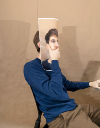 Image of adult male in a blue crewneck and khaki pants covering his face with a picture of his face with a hole for his nose to fit through.