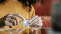 Image of a person's hands holding a crochet needle and working on a white yarn project.