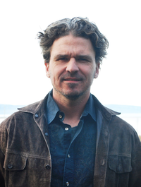 Dave Eggers standing outside wearing a brown jacket